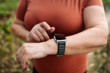 Portrait of a happy active beautiful senior caucasian woman runner running while checking heart rate at park, female in sport cloth jogging while looking on watch at park, healthy sport active