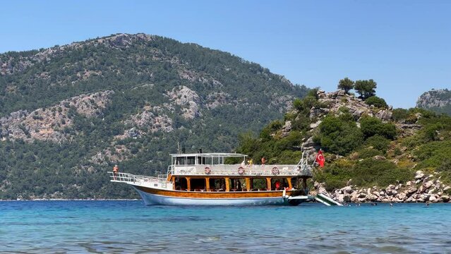 Cruise boat and swimmers at Cennet Bay in Marmaris looks like a dream from shore. Turquoise water, green forest and blue sky create a stunning contrast. Boat surrounded by peace and beauty, perfect es