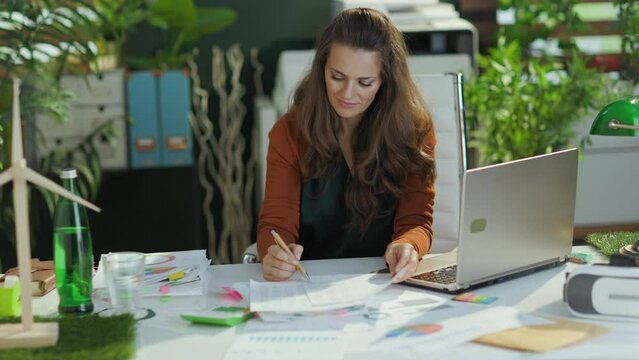 relaxed trendy 40 years old small business owner woman with laptop stretching in the modern green office.
