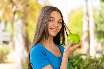 Teenager girl at outdoors holding an apple with happy expression