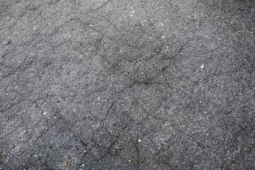 Broken grey asphalt road which is cracked. There are gravels on the black lines on the street. - Powered by Adobe
