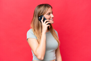 Young beautiful woman isolated on red background keeping a conversation with the mobile phone with someone