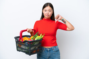 Young Asian woman holding a shopping basket full of food isolated on white background showing thumb down with negative expression