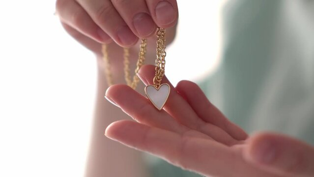Hand holding gemstone heart pendant on chain on white background, love and wedding concept