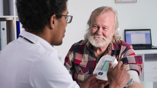healthcare, an elderly man at a reception at a young black doctor measures pressure with tonometer in medical cabinet