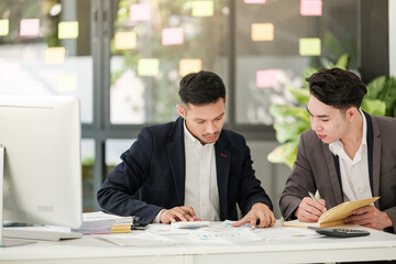 Smiling young businessman discussing something positive with his mature colleague, and using a digital tablet together