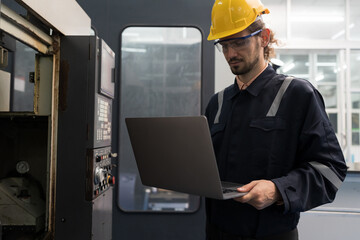 Male engineer worker working with laptop computer for control machine in the workshop. Male worker working with lathe machine with safety uniform and helmet in the industry factory
