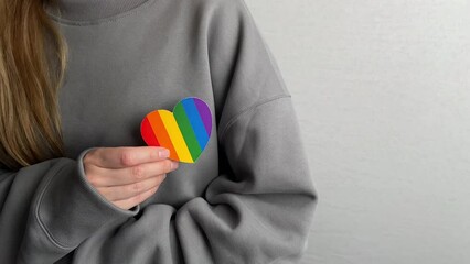 Woman holds in hands a heart in the colors of the rainbow. Young beautiful girl. LGBT history month. Pride Month. Lesbian Gay Bisexual Transgender. LGBT flag. Love, human rights, tolerance. LGBTQ+ - Powered by Adobe