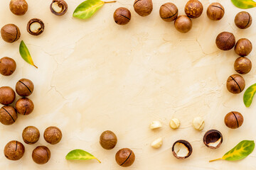 Shelled macadamia nuts with green leaves. Healthy snack background - obrazy, fototapety, plakaty
