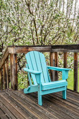 Fototapeta na wymiar empty Adirondack chair on a wooden backyard deck, spring scenery with a blooming apple tree