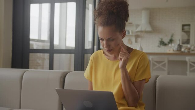 Pivoting around young adult African American woman in doubt browsing on her laptop