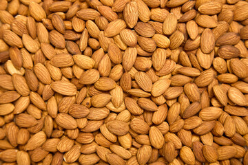 Background of brown large raw peeled almonds, arranged arbitrarily. A lot of delicious healthy almonds laid out in front of the camera, top view