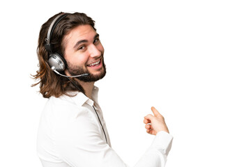 Telemarketer man working with a headset over isolated chroma key background pointing back