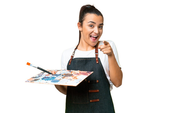 Young artist woman holding a palette over isolated chroma key background surprised and pointing front