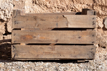 Back of old wooden box on rock. It has three horizontal slats. A slats is broken. Brown color.