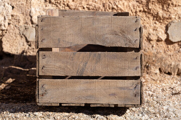 Side view of old wooden box on rock. It has three horizontal slats. Brown color.