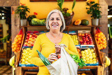 Happy senior woman buying fruits and vegetables at the market - Shopping food concept - 606545835