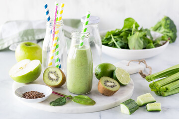 A bottle of green smoothie surrounded by ingredients used to make it.