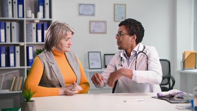 medical care, an elderly charming woman at consultation with an african american doctor complains about health while sitting in office