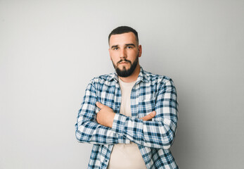 A man in a plaid shirt on a gray background crossed his arms over his chest. portrait of a serious...