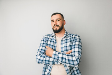 A man in a plaid shirt on a gray background crossed his arms over his chest. portrait of a serious...