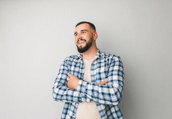 Fototapeta premium Confident young handsome man in shirt keeping arms crossed and smiling while standing against gray background