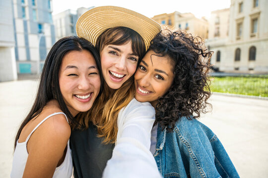 Multiracial three young women taking selfie portrait on city street - Happy female friends having fun together hanging outside - Life style concept with beautiful girls enjoying summer holidays