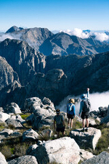 Hiking in the mountains with a group of hikers looking at the view of the mountains and clouds from the summit of a mountain.  - 606553252