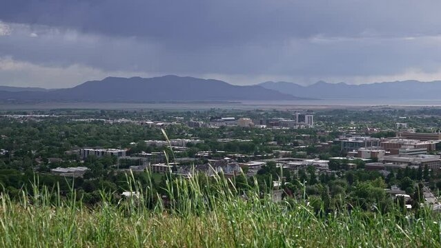 Panning view overlooking Provo city as grass blows in slow motion from view over Utah Valley.