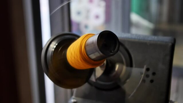 Close-up of a spinning yarn winder in the process of winding an orange woolen thread. Clothing and wool industry.