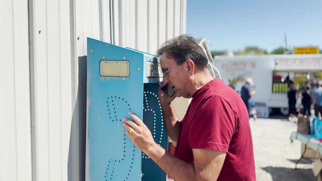 A man uses an old, outside phone booth to make a cellular phone call.  	