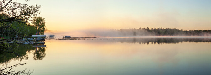 Panorama of a calm northern Minnesota lake and fog at dawn during spring with docks along the...