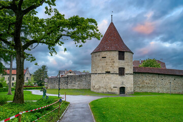 Fototapeta na wymiar Park view of Huwiler Tower in Zug, Switzerland at rainy spring evening. Huwiler Tower is the smallest of the four outer town wall towers in the city of Zug