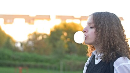 Curly-haired teenage girl inflates a big gum bubble until it bursts.