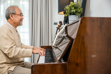 Happy relaxation Asian senior retirement man with eyeglasses learn to play piano at home, elderly old man playing music on piano in living room, lifestyle life after retirement, Close up hands © sorapop