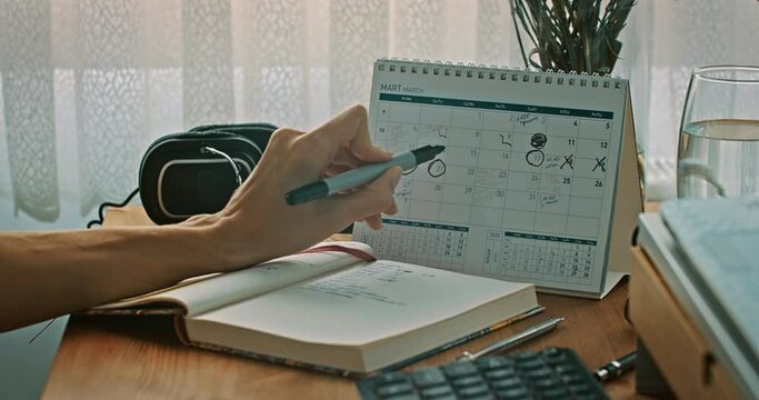 Woman marking dates on a calendar in home office, close-up