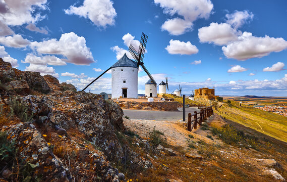 Wind mills and old castle in Consuegra, Toledo, Castilla La Mancha, Spain. Picturesque panorama landscape with road and view to ancient walls and windmills on blue sky with clouds