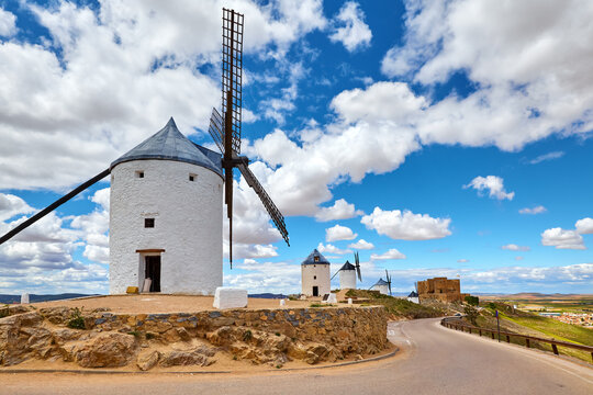 Wind mills and old castle in Consuegra, Toledo, Castilla La Mancha, Spain. Picturesque panorama landscape with road and view to ancient walls and windmills on blue sky with clouds