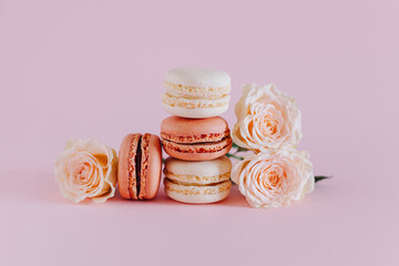 Obraz na płótnie Canvas Tasty french macarons with tender rose flowers on a pink pastel background.