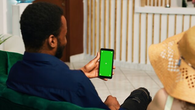 Tourists looking at greenscreen on phone, sitting in lounge area and using mockup template. Hotel guests waiting for check in procedure, holding smartphone with isolated display.