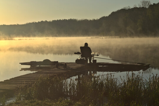 angler in the morning catches fish on a wooden pier
