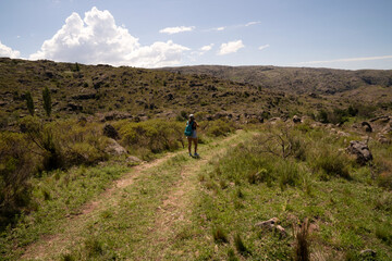 Fototapeta na wymiar Outdoor activities in a sunny day. View of a young woman walking along the hiking path across the hills and green grassland. 