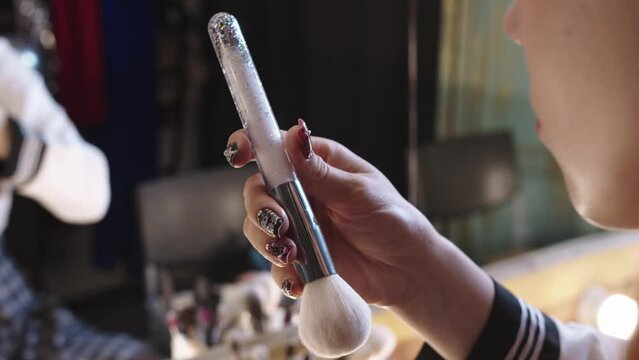 Young woman doing make up at the backstage - holding a brush with glitter in the handle
