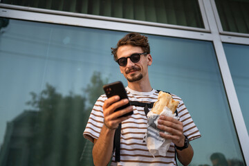 man caucasian tourist young adult eat sandwich and use mobile phone