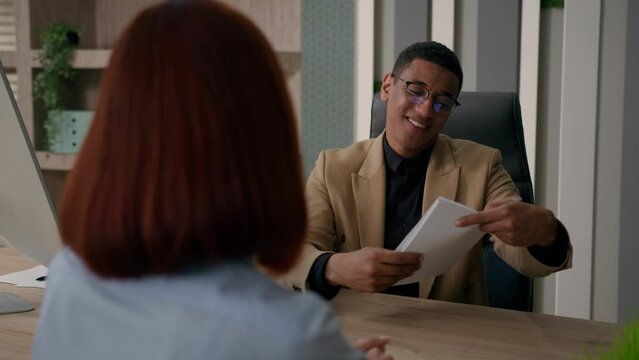 Smiling African American businessman man employer talk to woman hiring candidate job interview take resume business recruitment at workplace listen client at office meeting offer documents insurance