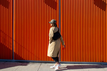 Girl on the street with an Orange background holding a coffee and looking away