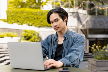 Portrait of smiling confident asian man, programmer using laptop computer working online project. Successful copywriter typing on keyboard sitting at workplace. Technology, successful business 
