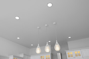 Ceiling with modern lamps and furniture in stylish kitchen, low angle view