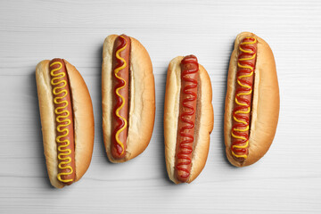 Fresh delicious hot dogs with sauces on white wooden table, flat lay