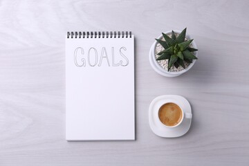 Notebook with word Goals, houseplant and cup of coffee on white wooden table, flat lay. Planning concept